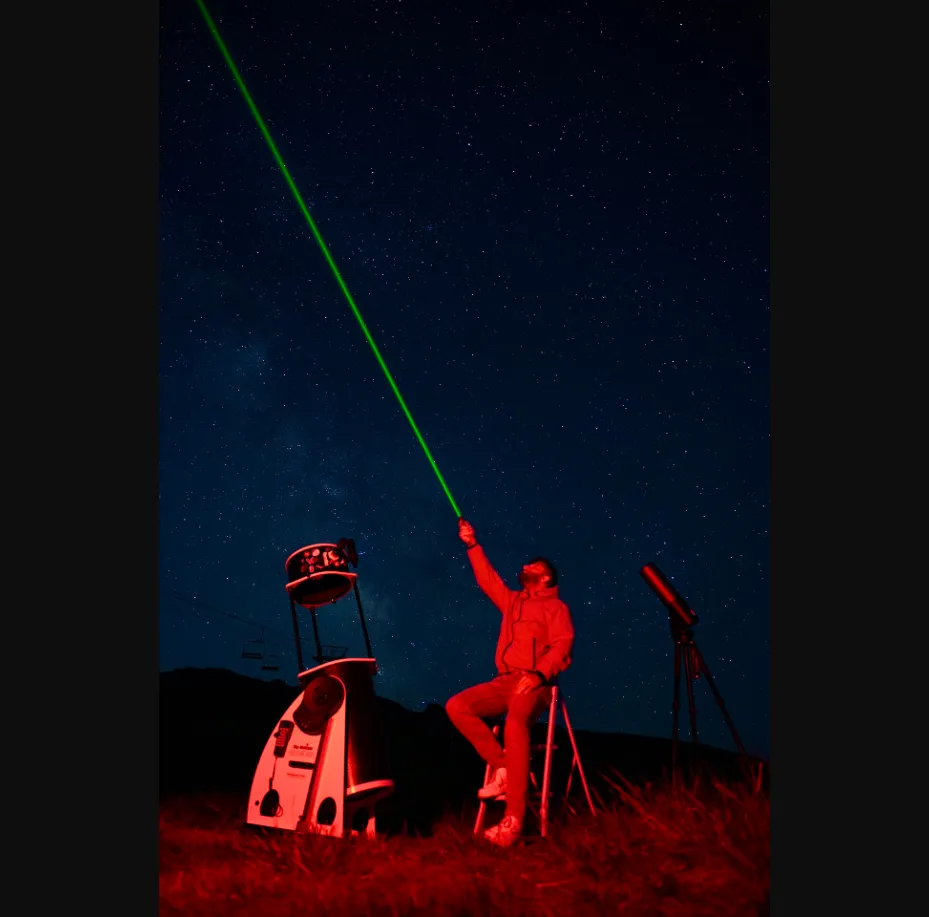 Astronomer with laser pointer and telescope under starry sky